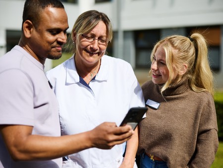 Drei Mitarbeiter:innen schauen gemeinsam auf ein Handy und tauschen sich aus. Foto: LWL/Matthias Haslauer